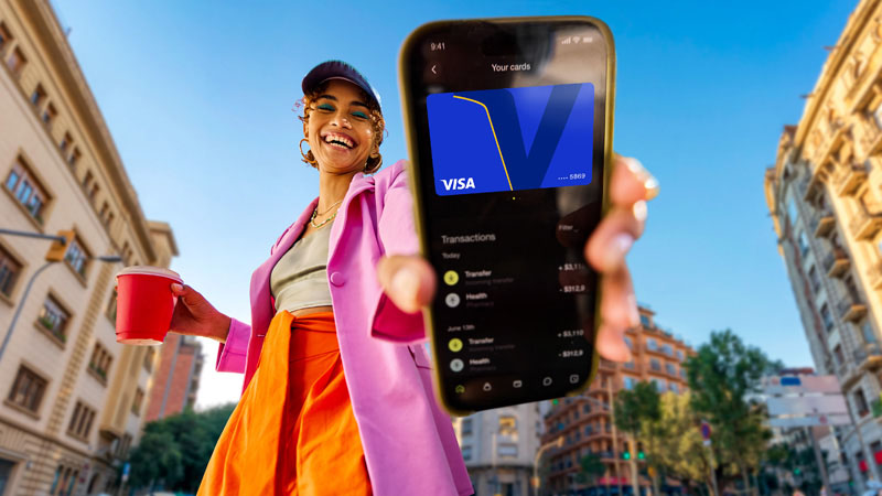 Young girl wearing a baseball cap and a hot pink trench coat holding a phone out as if to show us, a Visa card multisensory moment on her device