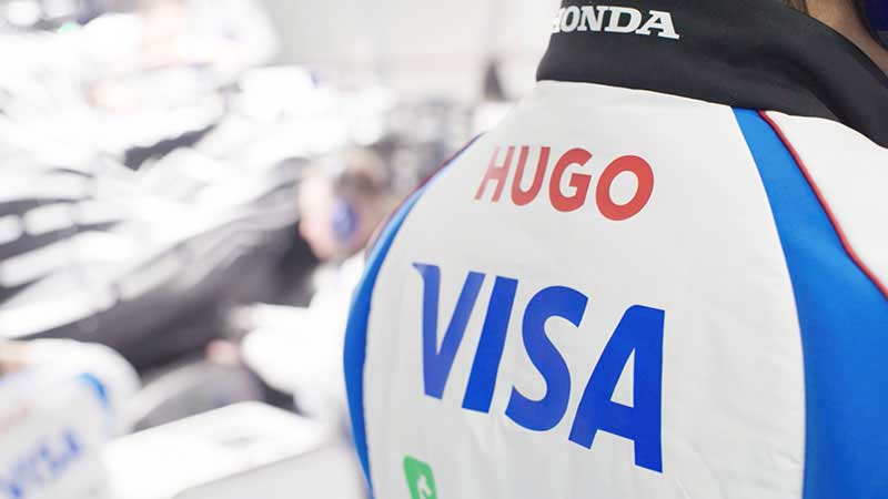 Zoomed in view of “HUGO” and “VISA” logos on the back of a driver jacket. 