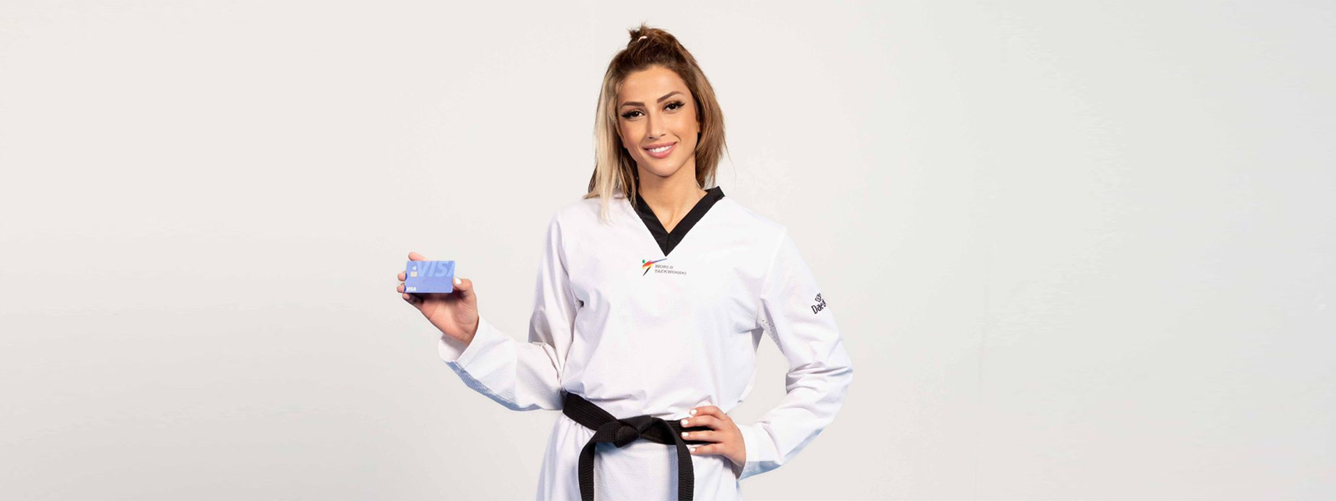Dina Pouryounes poses holding a Visa card while wearing a taekwondo uniform.