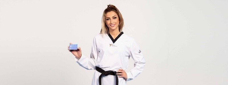 Dina Pouryounes poses holding a Visa card while wearing a taekwondo uniform.