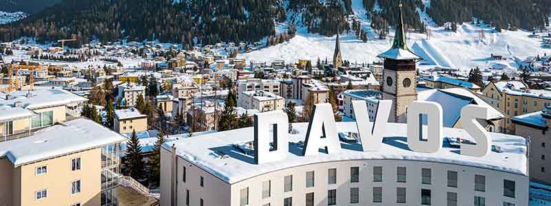 View of Davos, Switzerland with snow-covered buildings in the foreground and mountains in the background.