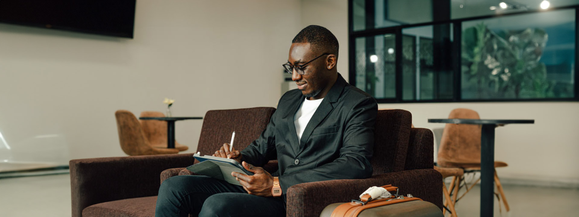 Man working on an ipad with a piece of luggage beside him.