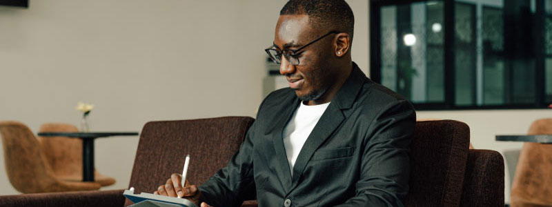 Man working on an ipad with a piece of luggage beside him.