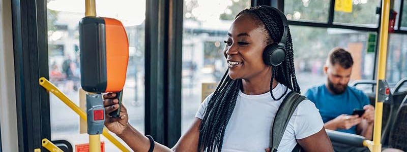 A woman, smiling and wearing headphones, taps her card to pay her fair on a city bus