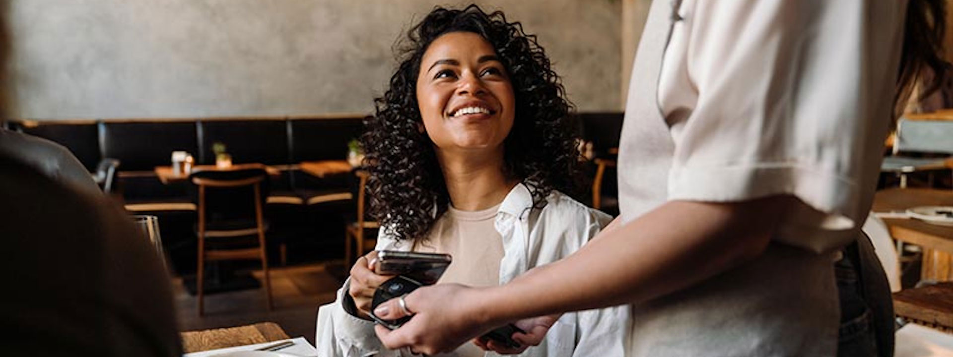 Woman using smartphone while paying restaurant bill with contactless payment during dinner party with friends