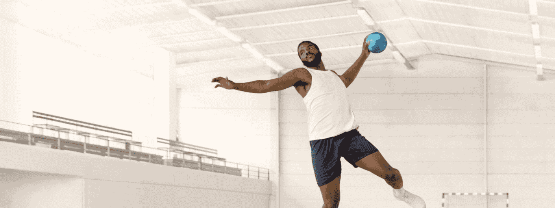 Handballer Dika Mem holding a handball mid-air while jumping in a white gymnasium.