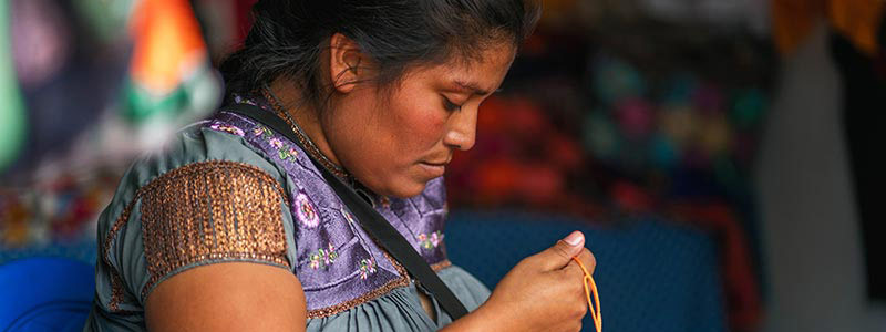 Small business owner in Central America crafting with colorful threads.