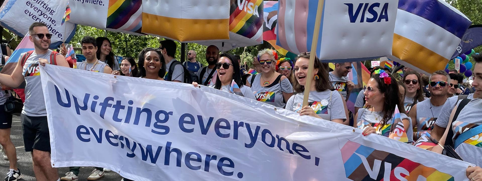 Visa employees wearing Pride flag shirts holding a banner that reads “Uplifting everyone, everywhere.”