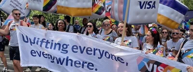 Visa employees wearing Pride flag shirts holding a banner that reads “Uplifting everyone, everywhere.”