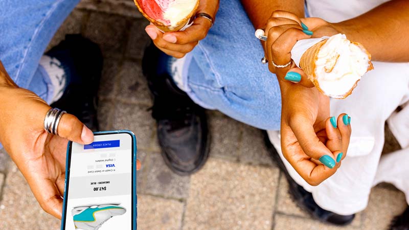 A close-up of two young friends sitting next to each other, looking at a product page of sneakers on a mobile device.