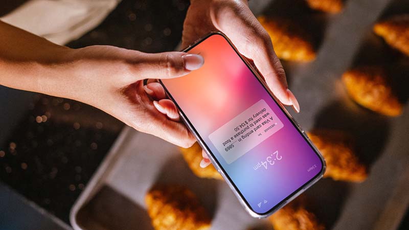 A young woman with pretty long nails holding up her phone to read a notification on the home screen of her device.
