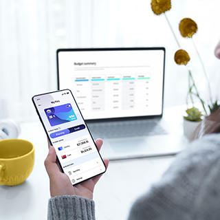 Person looking at transaction details on their phone at their desk. Visa logo can be seen on digital card in mobile screen.