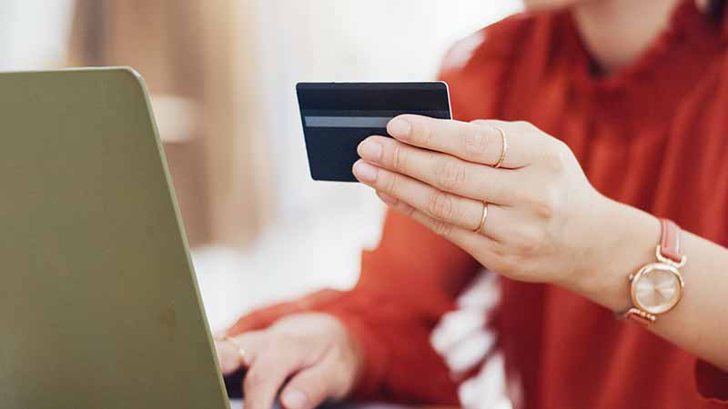 Close up of person holding up their credit card while using their laptop.