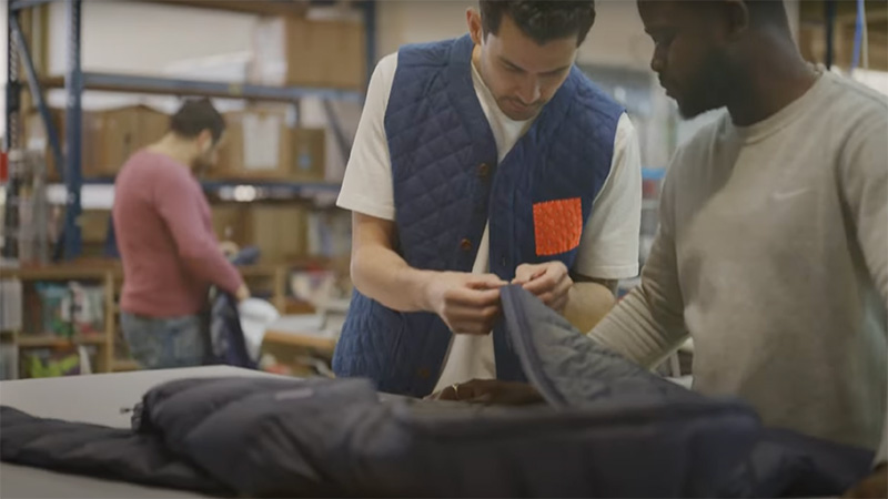 Two men collaborating on tailoring a jacket in a warehouse setting.