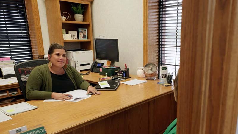 Smiling woman sits behind a large wood desk.