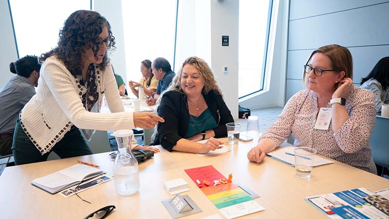 One waman teaching two other woman at a table in a conference room