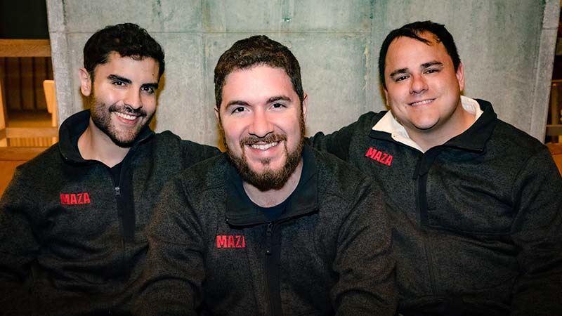 Robbie Figueroa, Luciano Arango, and Siggy Bilstein sit in a row wearing black pullovers with red Maza logos.