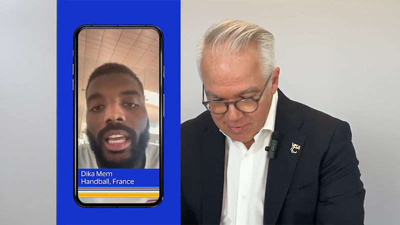 A man in a suit engaged in a phone conversation with French handball player Dika Mem