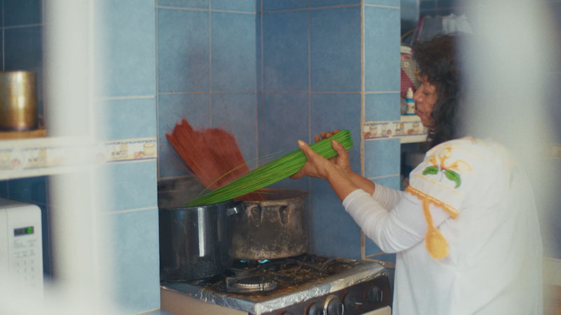 Woman dying bunches of poptillo green and red in big pots on a stovetop.