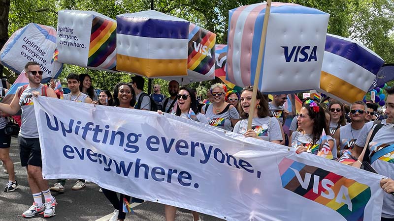 Visa employees wearing Pride flag shirts holding a banner that reads “Uplifting everyone, everywhere.”