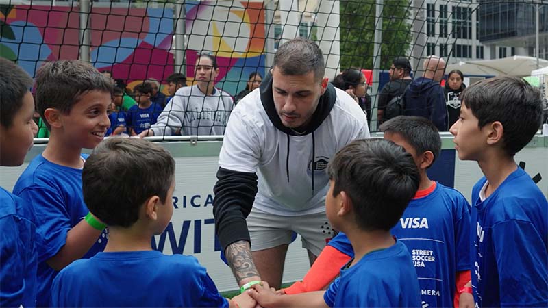 A coach surrounded by youth soccer players wearing blue shirts put their hands in for a cheer