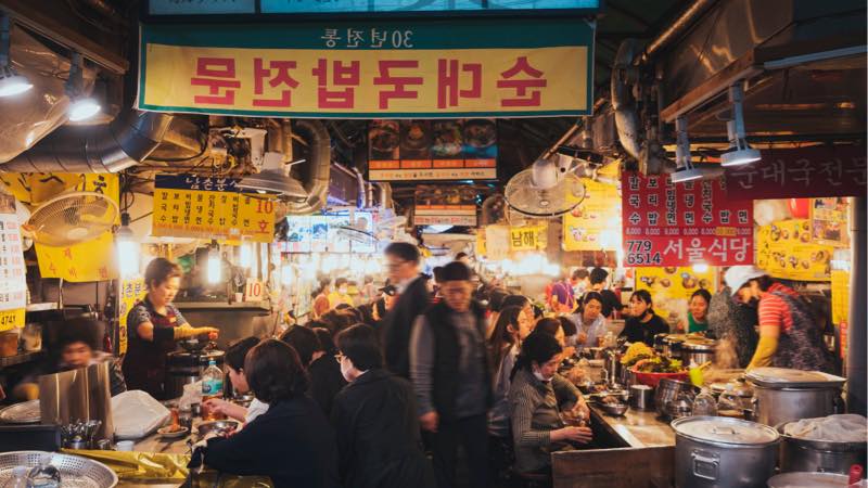 Crowded night food market in Asia with busy vendors and people exploring street food stalls.