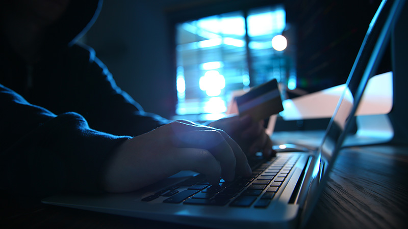 A fraudster using a laptop while holding a credit card